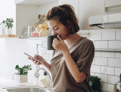 a woman viewing her mobile phone while drinking from a mug